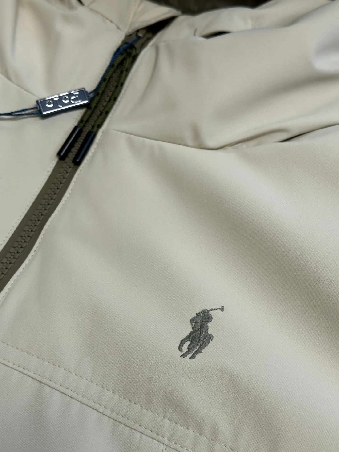 P970 Ralph Lauren logo hooded down jacket. The density of high-density nylon taffeta is about 210T-300T. The surface is smooth and slightly matte. It has excellent windproof and waterproof performance (with DWR water-repellent treatment). It has strong wrinkle resistance and is easy to care for. It is in line with the positioning of American casual "durable and practical".  The inner lining is made of 100% polyamide. The high-density and tight weaving process prevents fine lint from getting out of the gaps in the fabric. The smooth surface improves the putting on and taking off experience, and the excellent wear and tear resistance ensures damage caused by frequent use, while the light and soft texture does not affect the overall weight.  It uses 90 white duck down with a weight of 220g to ensure excellent thermal insulation performance. After strict screening and processing, the velvet is not easily drilled, ensuring durability. The classic jacket has a slightly loose fit, with slightly dropped shoulder lines (the shoulder width is 1-2cm wider than the standard fit). The length reaches the hips, and the sleeves are slightly tapered straight sleeves, taking into account freedom of movement and casual style.  The adjustable Velcro on the cuffs allows you to freely adjust the tightness according to the thickness of your wrist and personal preferences, effectively preventing cold wind from intruding, and improving the warmth performance. Two zippered pockets on the front are convenient for placing frequently used items, and the zipper design ensures that items are not easily lost. A built-in pocket on the left side of the chest provides a safe storage space for some small private items.  The drawstring design at the hem allows you to adjust the shape of the jacket according to your body shape and dressing needs. Whether it is loose and casual or slim and neat, you can easily control it.  Polo horse logo on the left chest: flat satin stitch embroidery (satin embroidery), using 100% polyester high color fastness embroidery thread (the color number is consistent with the brand's standard red color card), the stitch density is 12-15 stitches/cm, the outline of the horse logo is clear, and the details of the rider and horse are burr-free. Precise positioning through the template (12cm from the bottom of the collar and 8cm from the placket) ensures symmetry and centering.  size：s m l xl